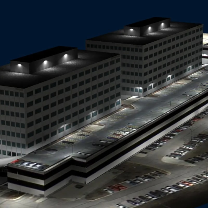 A nighttime view of two multistory office buildings with a large, well-lit parking garage and numerous parked cars, highlighting the effectiveness of photometric data in optimizing exterior lighting.